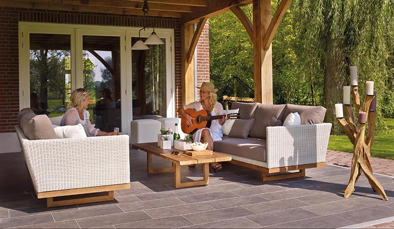 two couches on an outdoor patio, one person is playing guitar to another person